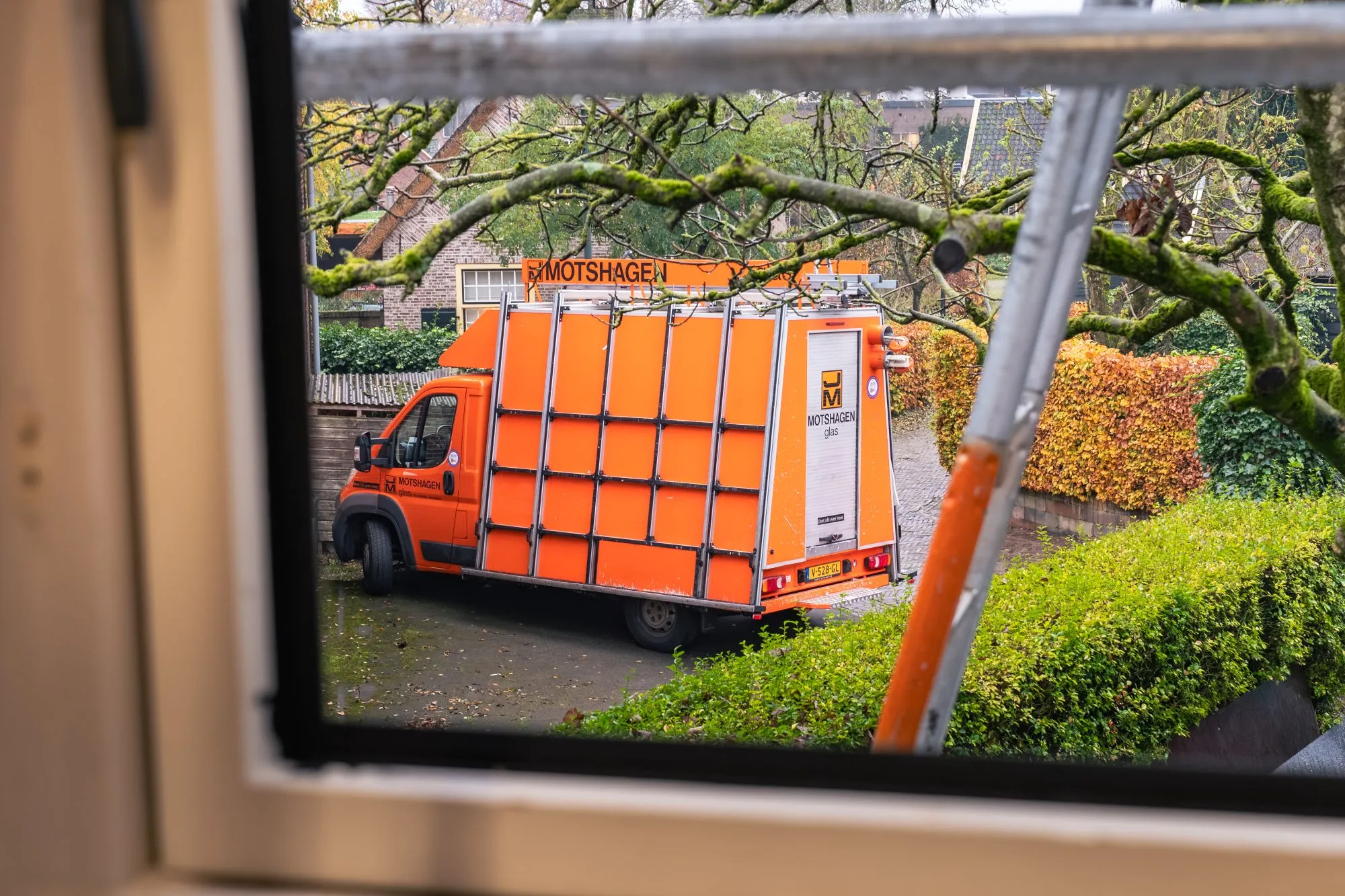 Bedrijfsbus Motshagen Glas Oranje bedrijfsbus van Motshagen Glas, gezien door een raam